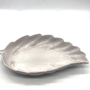 May include: A pale pink ceramic serving dish shaped like a leaf. The dish has a smooth, glossy finish and a slightly rippled edge.