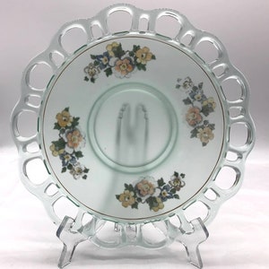 May include: A vintage green glass plate with a scalloped edge and a floral design. The plate has a white center with a gold rim and a floral pattern in shades of pink, yellow, and blue.