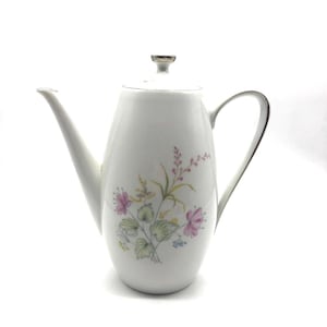 May include: White ceramic teapot with a floral design in shades of pink, green, and yellow. The teapot has a lid and a handle.