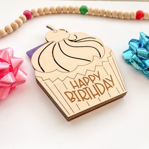 May include: A wooden cupcake card with the text "Happy Birthday" on it. The cupcake is decorated with a cherry on top and has a purple and white gift card inside.