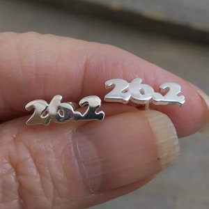 May include: A pair of silver stud earrings with the year 2022 written in a stylized font.