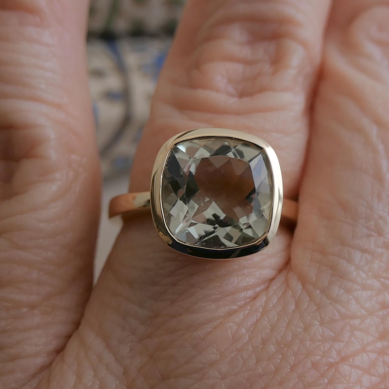 Puede incluir: Un anillo de oro con una gran piedra preciosa verde de talla coj&iacute;n engastada en un engaste de bisel.