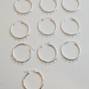 May include: Ten silver hoop earrings with five small rings hanging from each hoop.