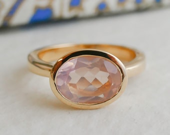 May include: A gold ring with a pale pink oval gemstone set in a bezel setting.