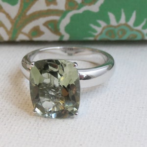 May include: A silver ring with a large, cushion-cut, green gemstone.