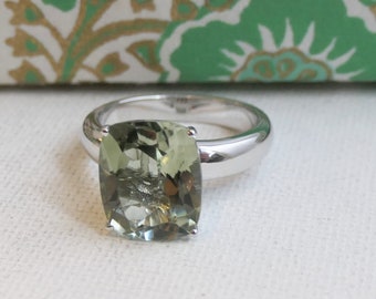 May include: A silver ring with a large, cushion-cut, green gemstone.