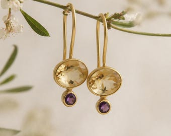 Pode incluir: Um par de brincos pendentes de ouro com uma grande pedra de citrino amarelo oval e facetada num engaste de ouro, com uma pedra de ametista roxa redonda e facetada mais pequena suspensa por baixo num engaste de ouro a condizer.