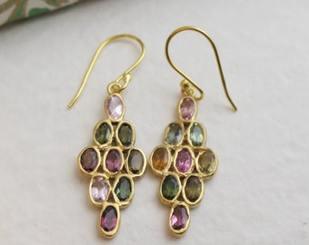 May include: A pair of gold-colored earrings featuring a cluster of oval-shaped gemstones in various colors, including pink, green, and brown. The earrings have a hook closure and a decorative design.