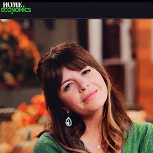 May include: A woman with brown hair and bangs wearing a green top and a pair of earrings. The logo "HOME ECONOMICS" is in green in the top left corner.
