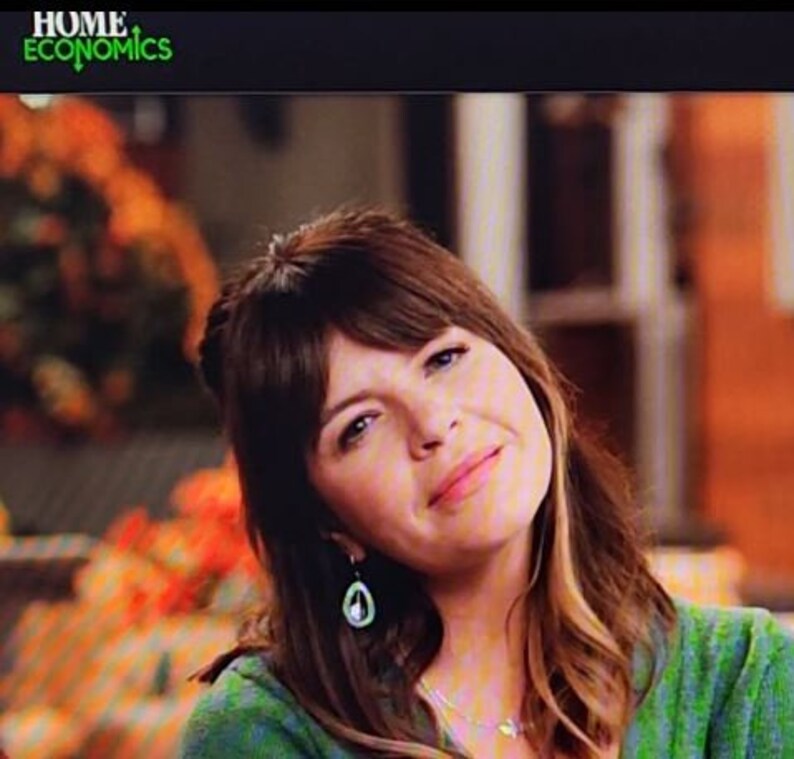 May include: A woman with brown hair and bangs wearing a green top and a pair of earrings. The logo "HOME ECONOMICS" is in green in the top left corner.