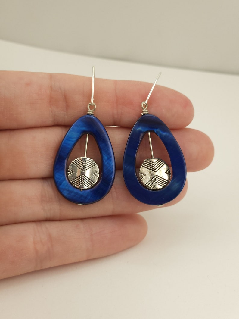 May include: A pair of teardrop-shaped earrings with a deep blue, marbled finish. Each earring features a silver-colored, circular accent with a geometric design suspended within the blue frame. The earrings have silver-colored hooks.