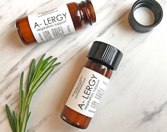 May include: Two amber glass bottles with black caps labeled "A-LERGY respiratory support" on a white marble surface. The bottles contain essential oils for respiratory support.
