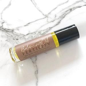 May include: A brown glass roller bottle with a black cap labeled "Balancing Oil FERTILITY" with the instructions "From menses through ovulation only. Inhale, apply to lower abdomen twice daily. Not intended for use during pregnancy."