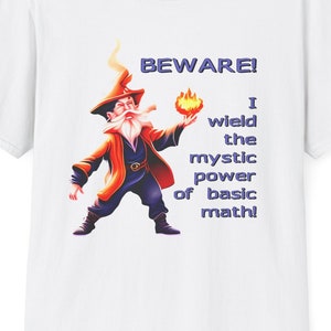 Puede incluir: Camiseta blanca con un diseño de mago de dibujos animados sosteniendo un orbe en llamas. El mago tiene una larga barba blanca. El texto en la camiseta dice "BEWARE! I wield the mystic power of basic math!" en azul.