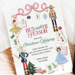 May include: A white invitation and a smartphone display the text "NUTerakER SEASON Christmas Mahjong." The invitation features illustrations of a ballerina, nutcracker, and other holiday-themed graphics. The smartphone is black.