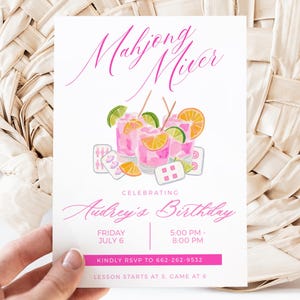 May include: A white invitation card with pink text and illustrations. The card reads "Mahjong Mixer" and "Celebrating Audrey's Birthday". It features watercolor illustrations of cocktails, dice, and mahjong tiles. The card is held in front of a woven fan.