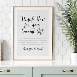 May include: A white framed sign with black text that reads "Thank You for your Special Gift. Your presence means the most to us! We will not be opening gifts at our shower. However, please let us know if you would like for us to open a gift with you. Thank You So Much!"