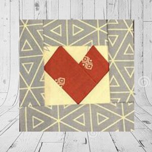 May include: A fabric block featuring a red heart design on a cream square, set against a grey background with a geometric pattern. The heart has a small square pattern. The background has a triangle pattern.