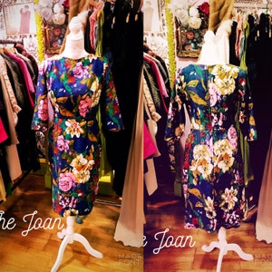 以下が含まれることがあります： ピンク、黄色、白の花柄が特徴の、ダークブルーのフローラルプリントドレス。 丸いネックラインと七分袖のデザイン。 白いマネキンに展示されています。 ヴィンテージ衣料品店に展示されているドレスです。