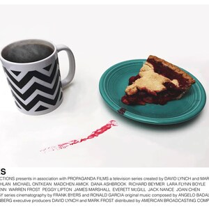 May include: A white mug with a black and white chevron pattern, filled with coffee, sits on a white surface. A slice of cherry pie on a teal plate is to the right of the mug. A red stain is on the surface between the mug and the plate. The text "TWIN PEAKS" is at the bottom of the image.