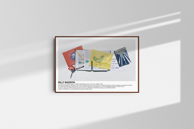 May include: A framed poster with a white background and the text "BILLY MADISON" in black. The poster features a still life of a yellow notebook, a red folder, a blue book, a yellow sheet of paper with a drawing of a duck, a pencil, and a pen.