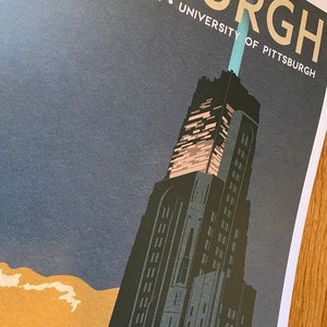 May include: A vintage-style travel poster featuring a tall, dark building with a blue and white light at the top. The building is set against a dark blue sky with a light brown cloud at the bottom. The text "Cathedral of Learning - University of Pittsburgh" is printed in yellow at the top of the poster.