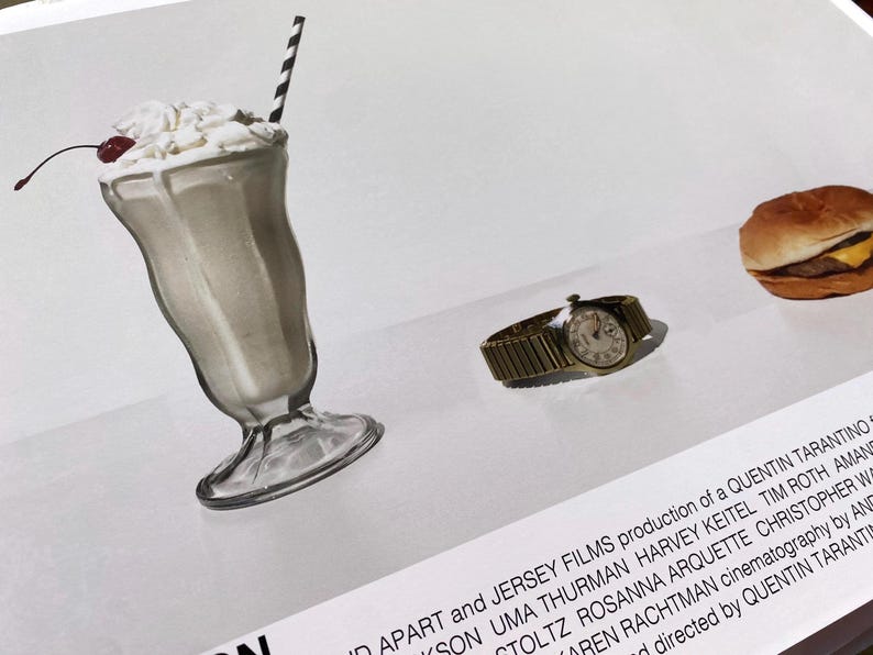 May include: A close-up of a movie poster for the film "Pulp Fiction". The poster features a milkshake, a watch, and a hamburger. The text on the poster reads "A production of a Quentin Tarantino film".