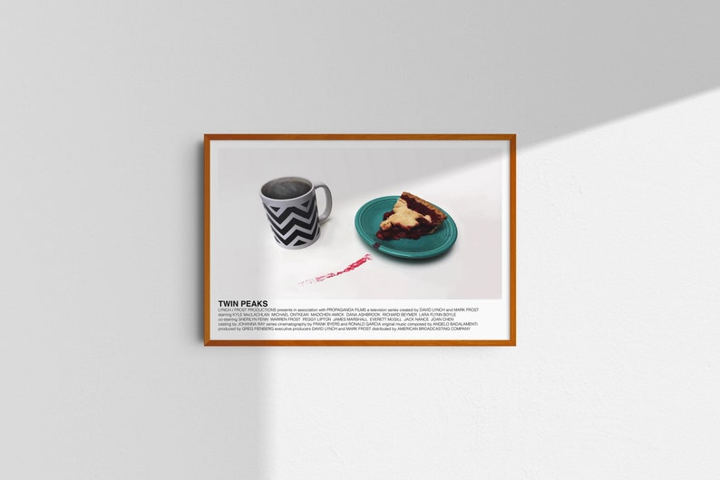 May include: A framed print of a white mug with a black chevron pattern and a slice of cherry pie on a teal plate. The print has the text "TWIN PEAKS" and credits for the show.