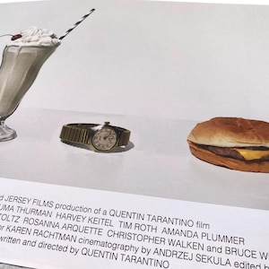 May include: A still life image of a milkshake, a wristwatch, and a hamburger. The milkshake is in a tall glass with a cherry on top and a striped straw. The wristwatch is gold with a white face. The hamburger is on a white plate. The image is a promotional poster for the film Pulp Fiction.