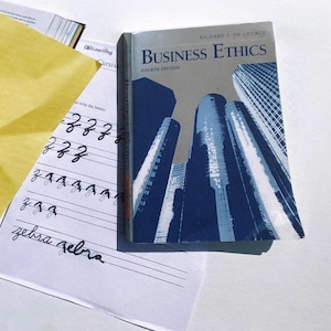 May include: A closed textbook titled "Business Ethics" by Richard T. De George, fourth edition. The cover features a blue and white illustration of skyscrapers.