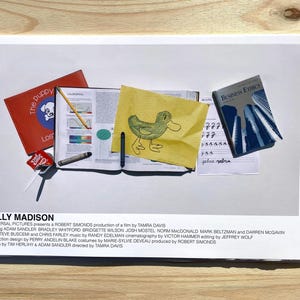 May include: A movie poster for the film "Billy Madison" starring Adam Sandler. The poster features a yellow sticky note with a drawing of a duck, a red book with the title "The Puppy", a blue book with the title "Business Ethics", and a few other school supplies.