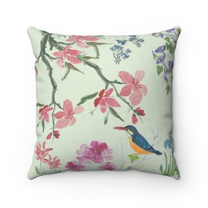May include: A green throw pillow with a watercolor design of pink flowers, blue flowers, and a blue and orange bird on a branch.