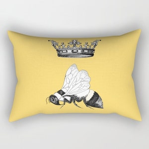 Pu&ograve; includere: Un cuscino rettangolare giallo con un'illustrazione in bianco e nero di un'ape e una corona. L'ape ha un addome a strisce e ali delicate. La corona &egrave; ornata, aggiungendo un tocco regale al design.