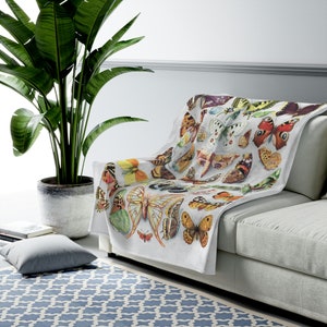 May include: A white throw blanket with a colorful butterfly pattern. The blanket is folded and draped over a white couch.
