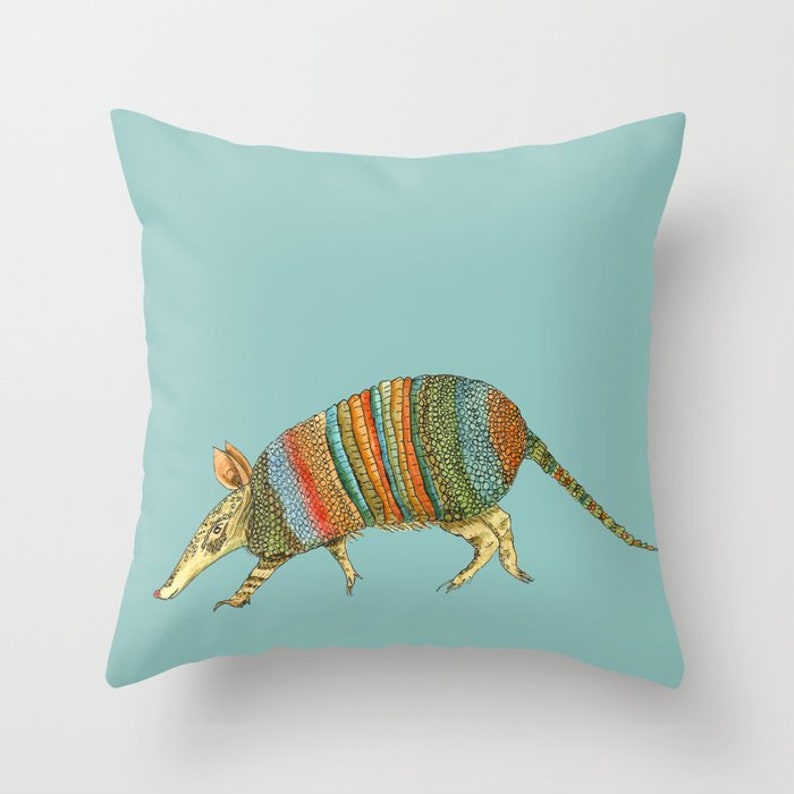 May include: A colorful illustration of an armadillo on a light blue background. The armadillo is walking to the right and has a striped shell with shades of orange, yellow, green, and blue.