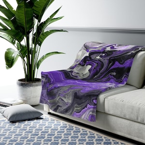 May include: Purple, black, and gray abstract throw blanket with a marbled design. The blanket is draped over a gray couch.