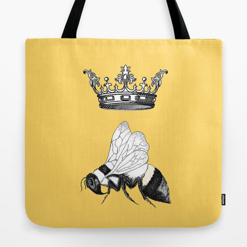 Pu&ograve; includere: Una borsa tote gialla con un'illustrazione in bianco e nero di un'ape e una corona. L'ape ha un addome a strisce e ali dettagliate. La borsa ha manici neri.