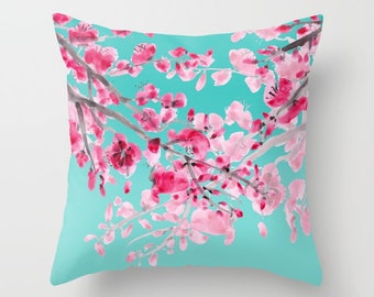 May include: A turquoise blue throw pillow with a watercolor design of pink cherry blossoms on a branch. The pillow is soft and comfortable and would add a touch of elegance to any room.