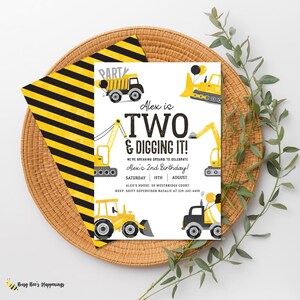 Può includere: Un invito di compleanno a tema costruzione. L'invito presenta illustrazioni di veicoli da costruzione gialli e il testo "Alex compie DUE anni e scava!" su sfondo bianco. L'invito è su un vassoio intrecciato con una busta a righe gialle e nere.