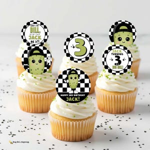 May include: Cupcakes with white frosting and decorative toppers. The toppers feature a cartoon pickle character wearing a cap, with text that reads "Happy 3rd Birthday Jack!" and "Jack Turning 3 is a Big Dill!"