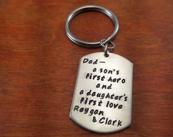 Puede incluir: Llavero de plata con una etiqueta que dice "Papá - el primer héroe de un hijo y el primer amor de una hija Reygan & Clark"