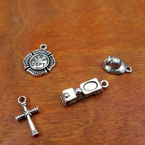 May include: Four silver-toned charms: a fire department badge, a fireman's hat, a cross, and a toy truck.