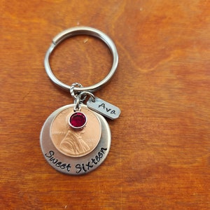 May include: Silver keychain with a penny, a red rhinestone, and a tag that says "Ava". The penny is dated 2007 and the tag is attached to a silver charm that says "Sweet Sixteen".