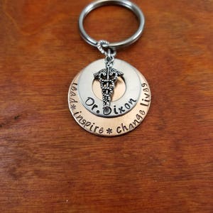 May include: Silver and copper keychain with a medical symbol charm. The keychain has the text "Lead * inspire * change lives" and "Dr. Dixon" engraved on it.