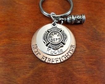 May include: Silver keychain with a fire department emblem, the words "Hot Firefighter" and the name "Kuche" engraved on it. A small silver fire hydrant charm is attached to the keychain.