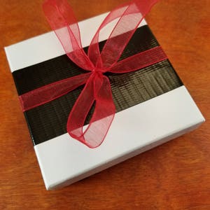 May include: A white gift box with a black and white striped ribbon and a red sheer bow.