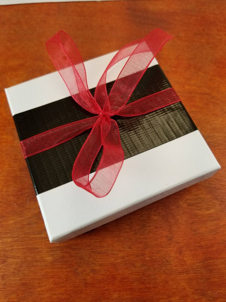 May include: A white gift box with a black and white striped ribbon and a red sheer bow.