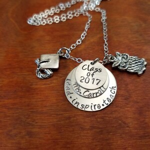 May include: Silver necklace with a graduation cap charm, a round charm with the text "Class of 2017", a round charm with the text "Ms. Carroll", and a round charm with the text "lead. inspire. teach", and an owl charm.