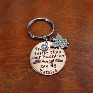 May include: A copper-colored keychain with a silver angel charm and a clear rhinestone. The keychain has the text "Never drive faster than your Guardian Angel can fly Natalie" engraved on it.