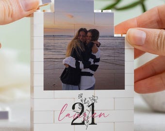 May include: A rectangular construction block display featuring a printed photograph of two people embracing on a beach at sunset. Below the photo, the white block surface displays the name Lauren in pink script and the number 21 in black.